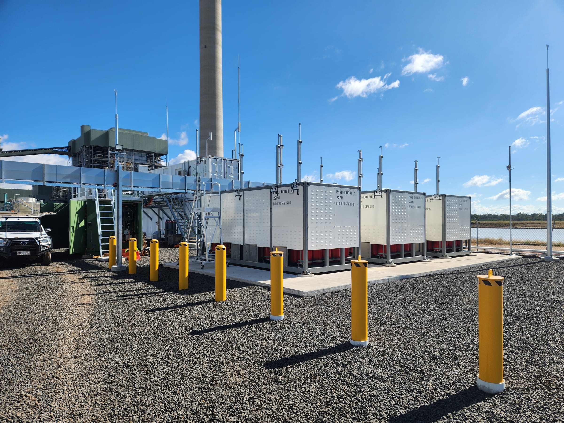 Equipment containers and safety bollards on a finished site beside a tall stack