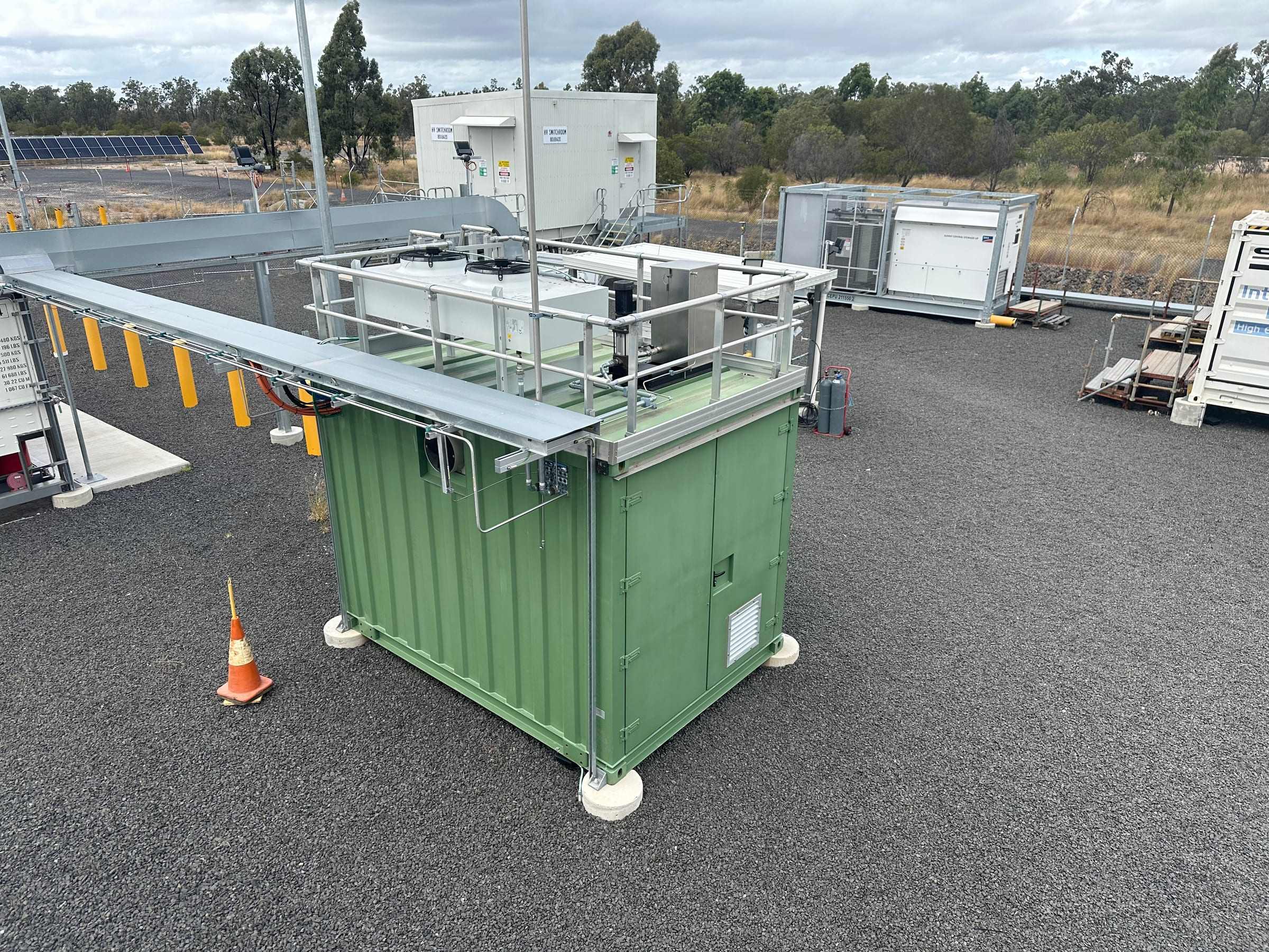 Newly installed green equipment enclosure with access platform on a gravel site